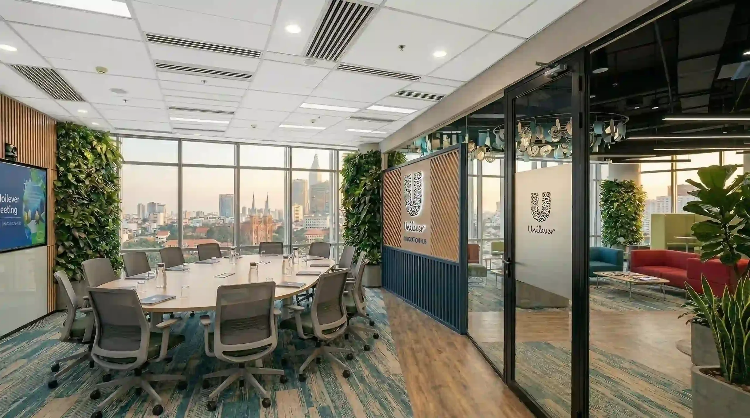 Góc nhìn từ ngoài vách kính vào phòng họp lớn của Unilever, hiển thị bàn họp, dãy ghế lưới xám và cảnh quan Nhà thờ Đức Bà.